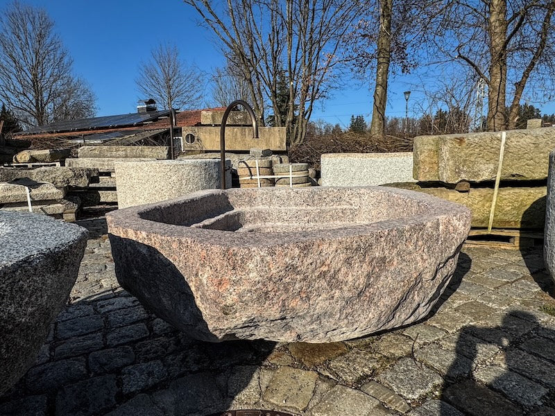 Findlingsbrunnen mit dunklen und rosa Einschlüssen und Handrad