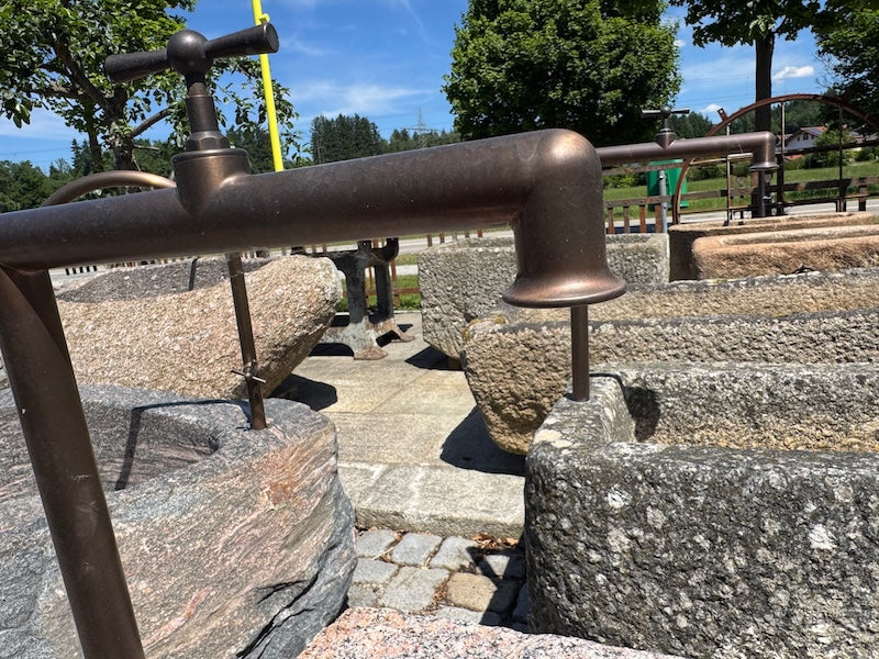 Findlingsbrunnen mit dunklen und rosa Einschlüssen und Wasserhahn