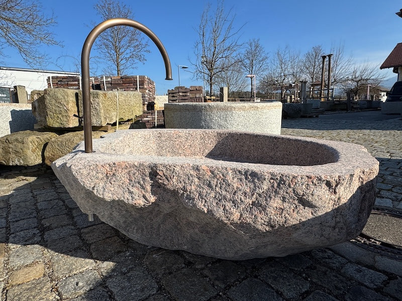 Findlingsbrunnen mit dunklen und rosa Einschlüssen und Wasserauslauf