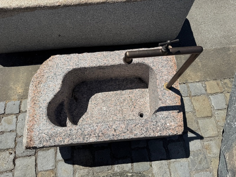 Findlingsbrunnen mit dunklen und rosa Einschlüssen und Wasserauslauf