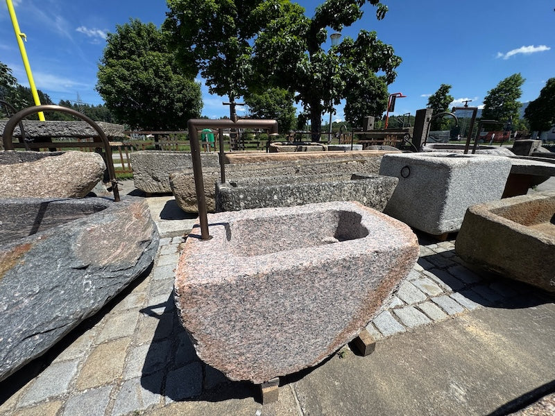Findlingsbrunnen mit dunklen und rosa Einschlüssen und Handrad