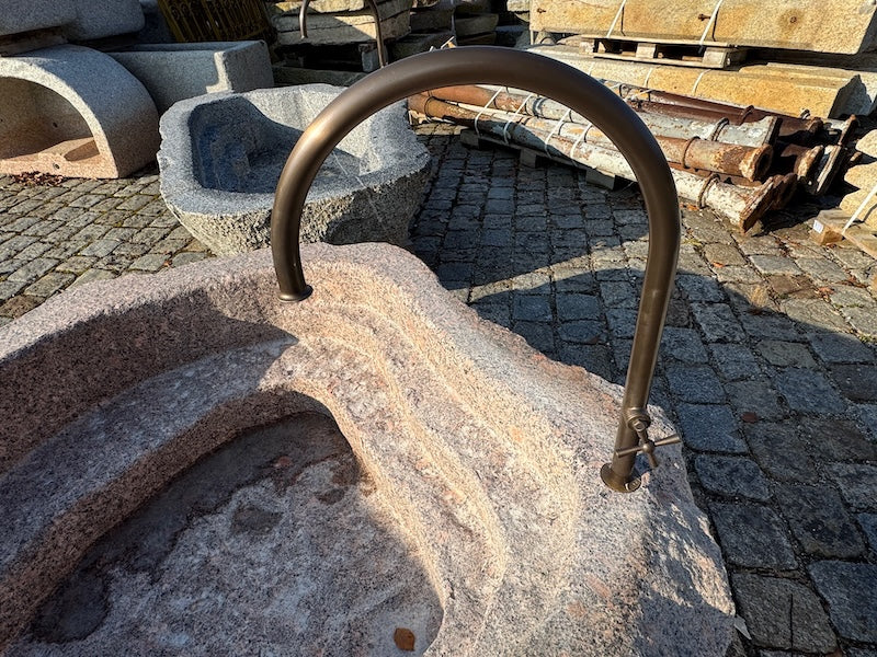 Findlingsbrunnen mit dunklen und rosa Einschlüssen und Wasserhahn