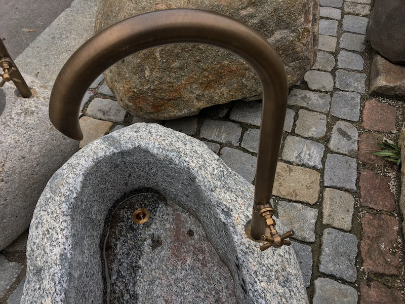 Kleiner Findlingsbrunnen mit farblichen Einschlüssen und Wasserhahn